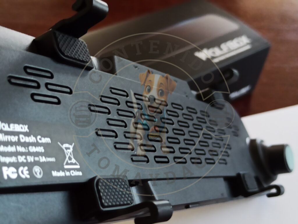 Imagen de la parte trasera de una dashcam Wolfbox modelo G840S, mostrando los detalles de ventilación, sujeción y especificaciones técnicas. En segundo plano se aprecia la caja original del producto. Marca de agua visible de Tomaydaca.